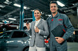 Beautiful businesswoman with keys shows thumb up and auto service mechanic with documents. Car repair and maintenance.