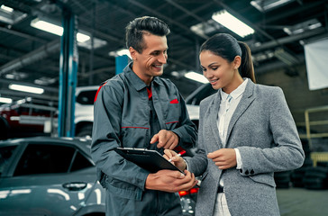 Beautiful businesswoman and auto service mechanic are discussing the work and signing documents. Car repair and maintenance.