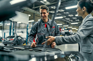 Beautiful businesswoman and auto service mechanic are discussing the work. Car repair and maintenance.