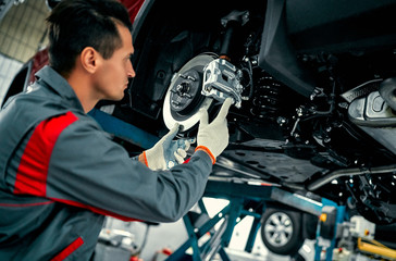 Wall Mural - Car mechanic worker repairing suspension of lifted automobile at auto repair garage shop station