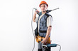 A builder with a hammer drill on his shoulder, and a angle grinder in his other hand, in a helmet, smiles.