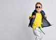 Attractive little boy in stylish warm clothes with a backpack on his shoulders, having fun on a light studio background.