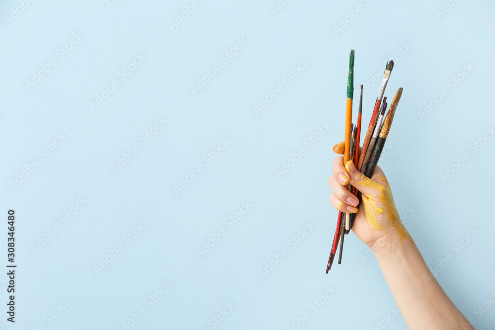 Hand of artist with brushes on color background - obrazy, fototapety, plakaty 