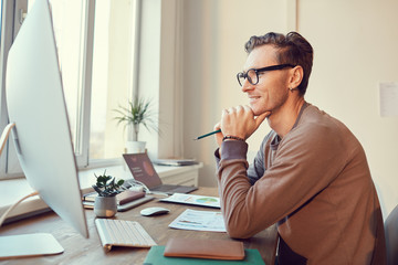 Side view portrait of adult businessman looking at computer screen and smiling while working at desk in modern office, copy space
