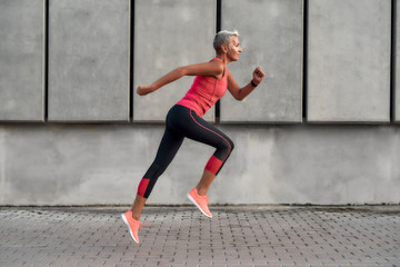 full of energy. side view of active middle aged woman in sport clothing jumping while exercising out