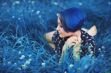 Millennial girl with blue hair. Beautiful young stylish close eyes woman lying down and rest on grass in summer time in the park. Fresh natural summer peace view. Classic blue 2020 year color concept