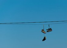 Old Ripped Sneakers Hang On Electric Wires Against The Blue Sky In The City. Hooliganism..