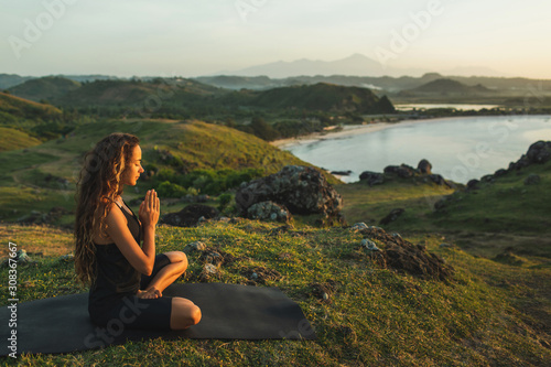 Woman doing yoga alone at sunrise with mountain and ocean view. Harmony with nature. Self-analysis and soul-searching