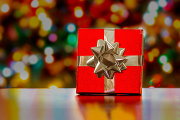 Red gift present box on a table with a christmas tree and lights