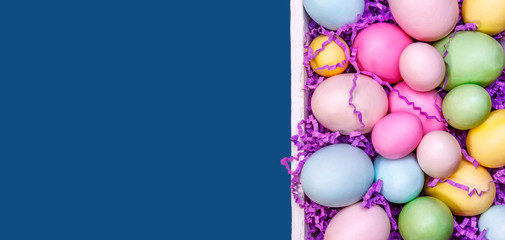 Wall Mural - Multicolor eggs in a white tray. Creative Easter concept. Modern solid classic blue background. Horizontal, banner format