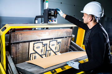 Turning on a punching machine. Worker in a hard hat in cardboard boxes factory working on paper die cutting machine.