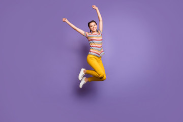 Poster - Full size photo of funny lady jumping high summer mood enjoy sunny day raise hands fists wear casual striped t-shirt yellow trousers isolated purple color background