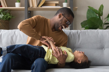 Wall Mural - Happy african American dad laughing playing with son at home