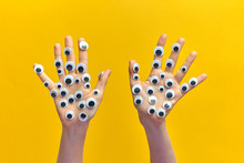Two Girl's Hands With Plastic Eyes On An Yellow Background.