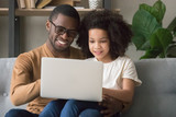 Fototapeta Tulipany - Smiling black dad and daughter use laptop at home