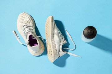 Wall Mural - White sneakers and a bottle of water under morning sunlight on a blue background.Jogging, running, fitness, cross fit, hard workout. Morning run. Banner. Flat lay, top view