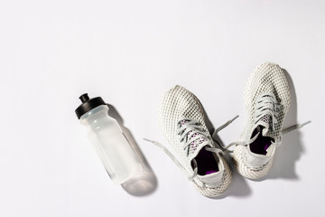 Wall Mural - White sneakers and a bottle with water under morning sunlight on a white background. Concept, jogging, running, fitness, cross fit. Morning run. Banner. Flat lay, top view