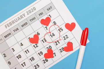 Valentine's day 14 is marked with a heart on the calendar, paper hearts and a felt-tip pen are scattered around. Holiday concept