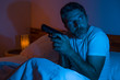 © TheVisualsYouNeed - night edgy portrait of young stressed and paranoid American man lying on bed unable to sleep holding gun looking around scared suffering paranoia expecting intruders