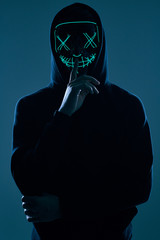 Wall Mural - Anonymous man in black hoodie hiding his face behind a neon mask