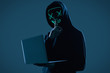 Anonymous man in a black hoodie and neon mask hacking into a computer