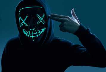 Wall Mural - Anonymous man in black hoodie hiding his face behind a neon mask
