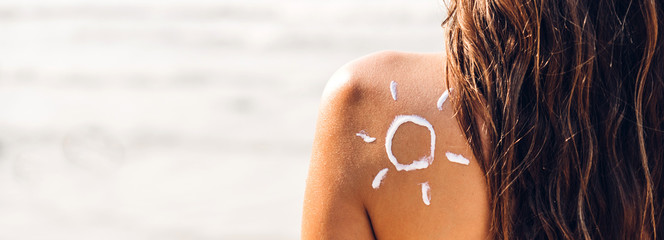 Woman wearing two piece bikini applying suncream with sun drawn on back on the tropical beach.Summer vacations