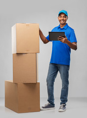 Wall Mural - mail service, technology and shipment concept - happy indian delivery man with boxes and tablet computer in blue uniform over grey background