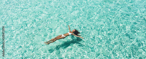 Fotografía Woman in white bikini lying on transparent turquoise water surface on beach