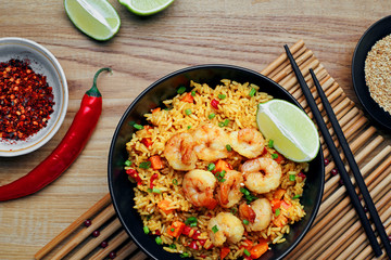 Wall Mural - Classic Shrimp Fried Rice with fresh shrimp, rice, green onions, vegetables and lime in a bowl. Healthy Thai food on a wooden table. Top view, directly above shot.