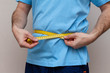 © vitalis83 - man in a blue T-shirt measures the waist with a yellow tape