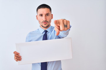 Poster - Young business man holding blank banner over isolated background pointing with finger to the camera and to you, hand sign, positive and confident gesture from the front