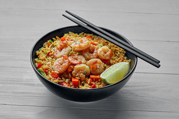 Wall Mural - Classic Shrimp Fried Rice with fresh shrimp, rice, green onions, vegetables and lime in a bowl. Healthy Thai food on a white wooden table.