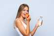 © luismolinero - Young blonde girl with an apple and with a bottle of water over isolated background