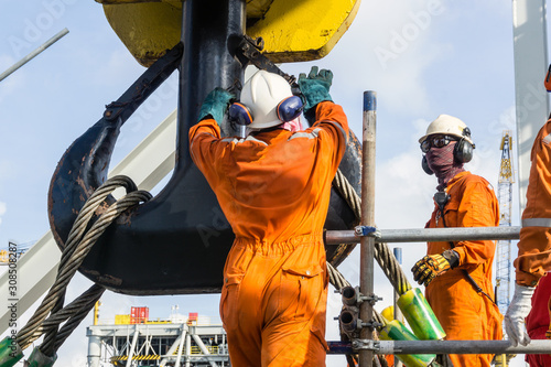 Offshore workers installing a heavy lifting sling onto a crane hook on board a construction work barge at oil field