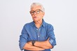 Senior grey-haired woman wearing denim shirt and glasses over isolated white background skeptic and nervous, disapproving expression on face with crossed arms. Negative person.