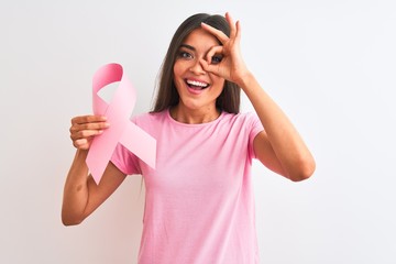 Wall Mural - Young beautiful woman holding cancer ribbon standing over isolated white background with happy face smiling doing ok sign with hand on eye looking through fingers