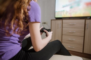 Happy woman playing video games, sitting on bed holding joystick.