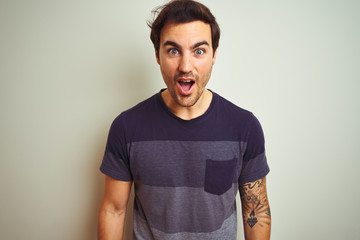 Wall Mural - Young handsome man with tattoo wearing casual t-shirt over isolated white background afraid and shocked with surprise expression, fear and excited face.