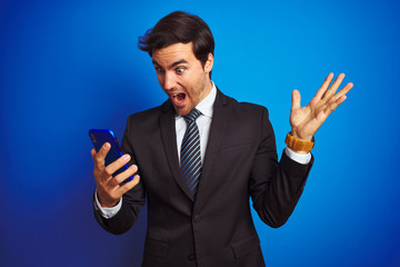 Sticker - Young handsome businessman using smartphone standing over isolated blue background very happy and excited, winner expression celebrating victory screaming with big smile and raised hands