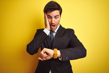 Wall Mural - Young handsome businessman wearing suit and tie standing over isolated yellow background Looking at the watch time worried, afraid of getting late