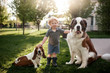 © Cavan Images - Toddler boy standing grass with 2 dogs in backyard in pretty light