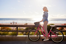 Side View Of Senior Woman With Bicycle Standing On Road At Manhattan Beach Against Sky During Sunny Day