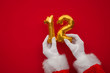 © ink drop - 12 days of christmas. Santa hands holding 12th day balloon on red background