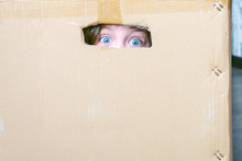  The Baby Hid In A Cardboard Box And Is Afraid. A Child With Wide Open Eyes Sits In A Mail Box. The Frightened Blue Eyes Of A Little Girl Are Visible Through A Gap In Cardboard.