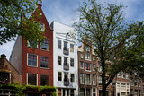 Fototapeta Big Ben - View of historical, traditional and typical buildings showing Dutch architectural style and trees in Amsterdam. It is a sunny summer day.