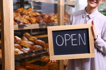 Wall Mural - Female business owner holding OPEN sign in bakery, closeup