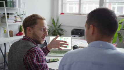 Wall Mural - Panning shot of two web designers working on application interface for various devices. Creative professionals discussing samples presented on laptop screen sitting at desk in office