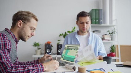 Wall Mural - young designer or marketing manager joining colleague working on laptop at desk and showing him idea