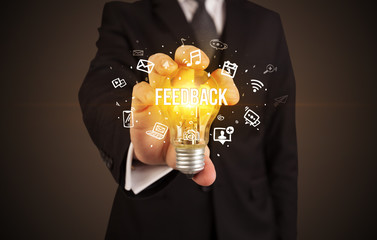 Businessman holding light bulb with FEEDBACK inscription, social media concept